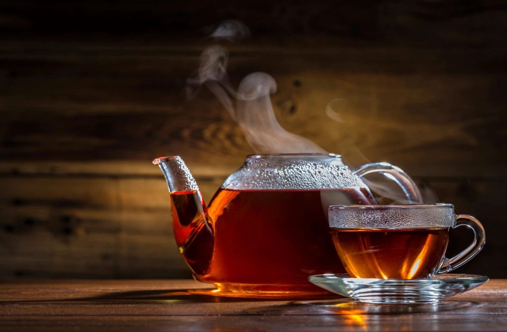 Steaming teapot and cup of tea on wood table.