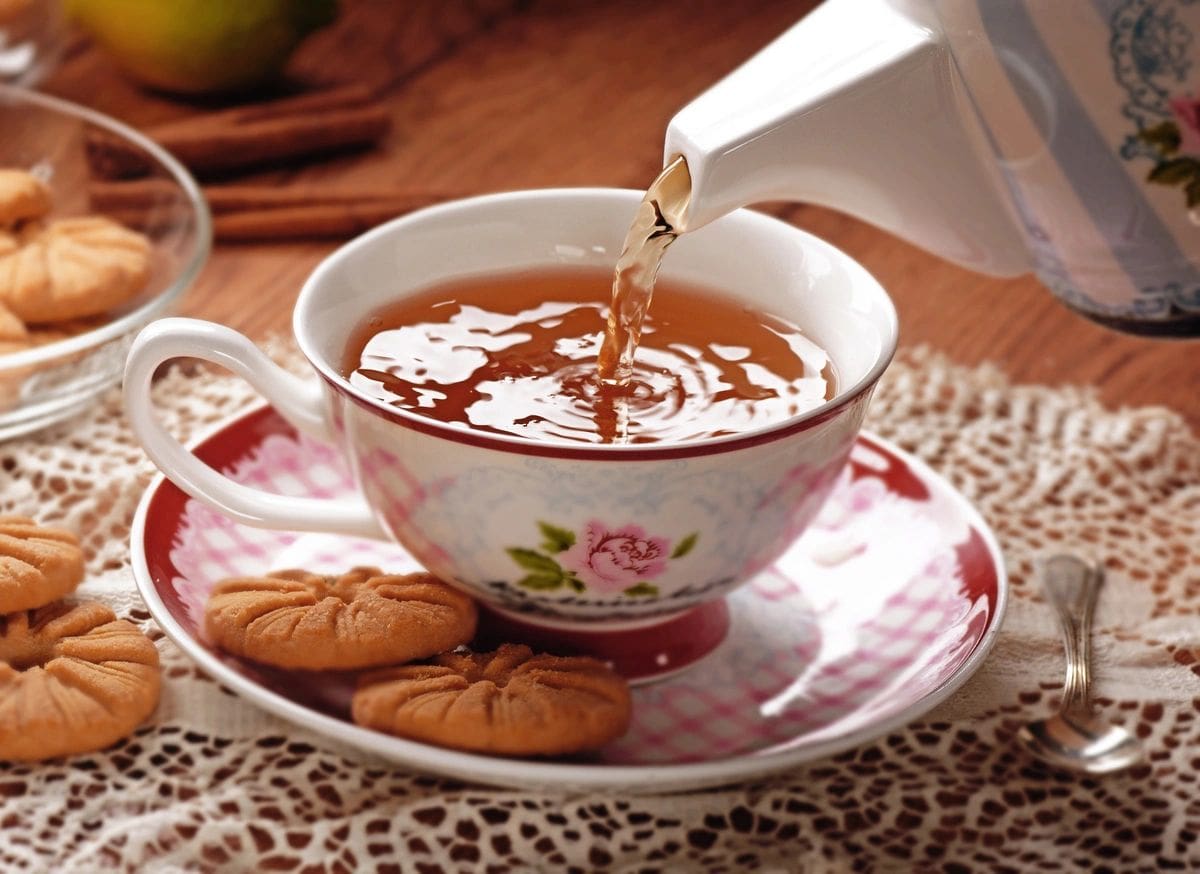 Tea pouring into a floral teacup with cookies.