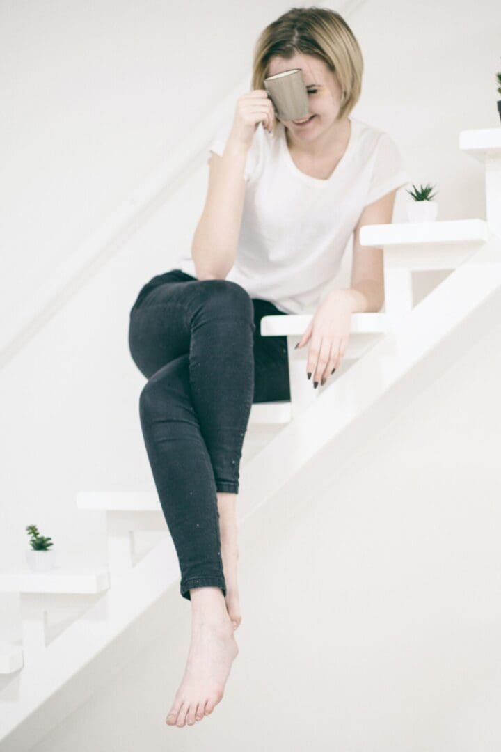 A woman holding a cup sitting on the staircase