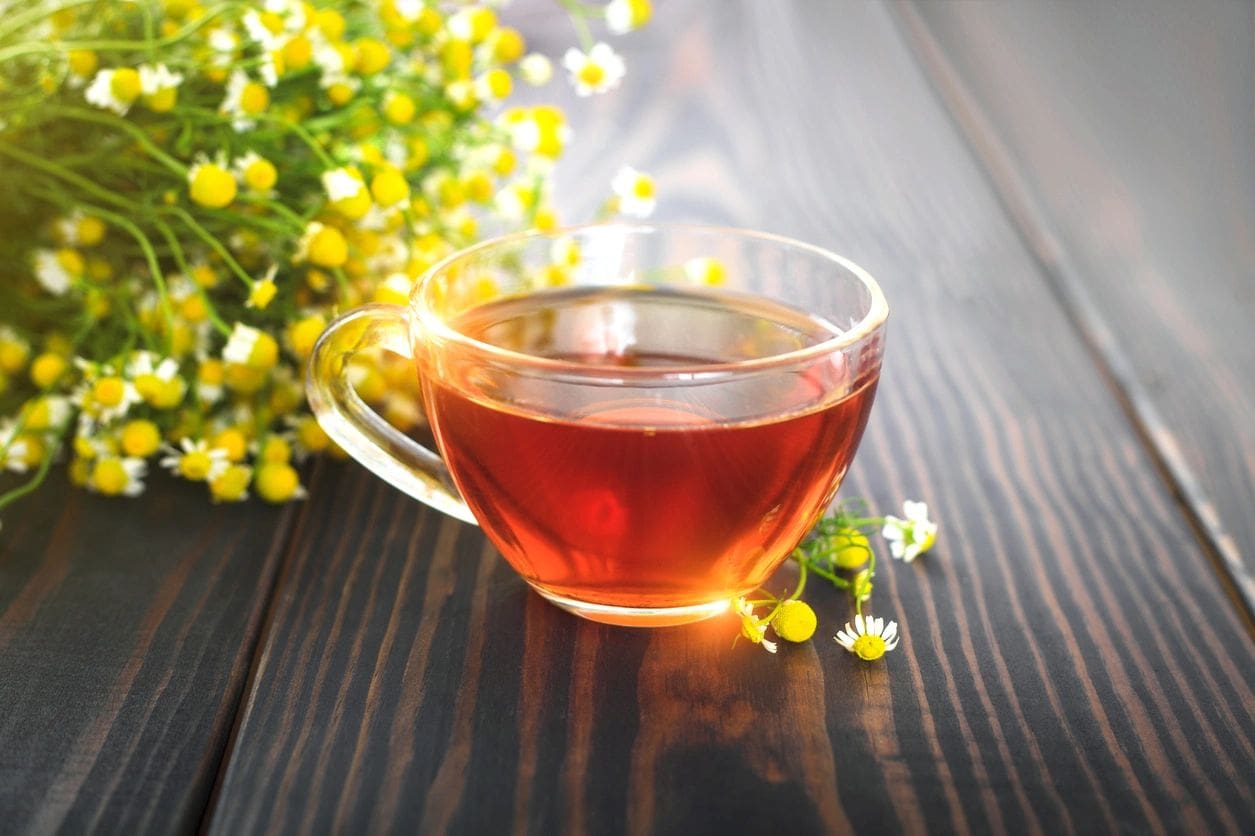 Chamomile tea in a glass cup on wood.