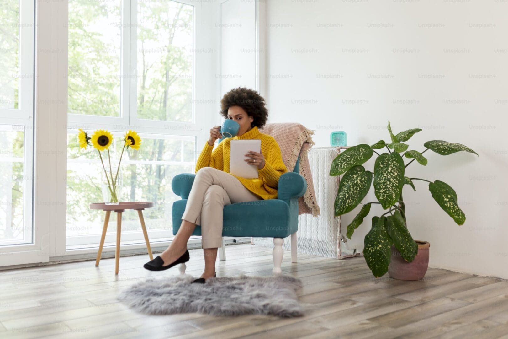 Woman in yellow sweater reads tablet in chair.