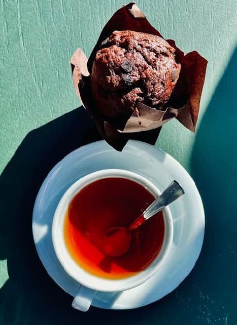 A cup of tea and a chocolate muffin on a saucer.