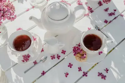 Two cups of tea and teapot on a table with flowers.